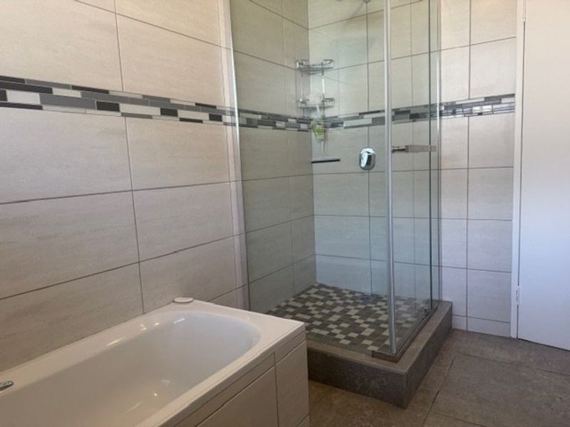 A clean, modern bathroom featuring a built-in bathtub and a separate glass-enclosed shower with neutral wall and floor tiling.