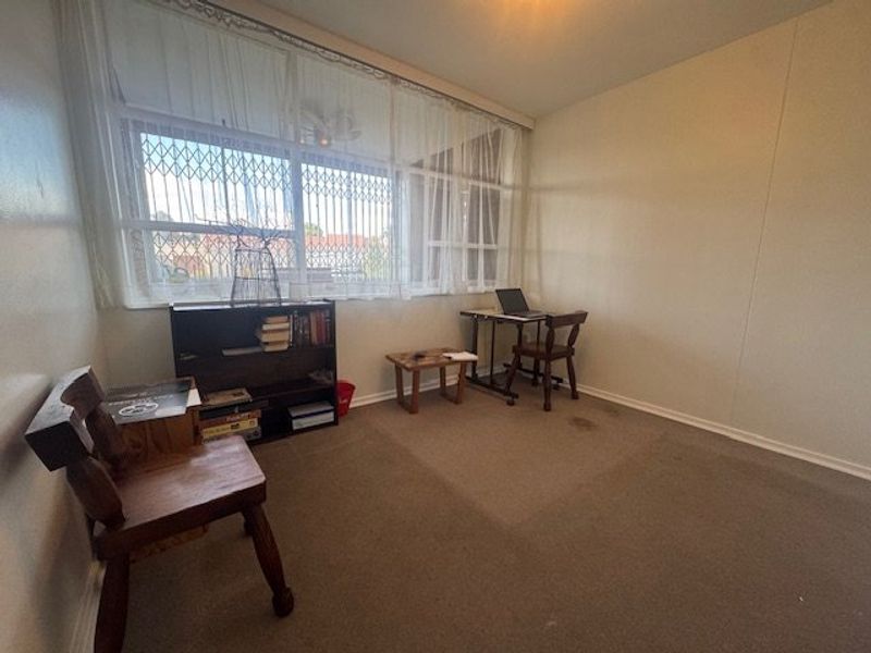 A bedroom featuring a large window with security gate and carpeted flooring, offering a functional space ready for updates.
