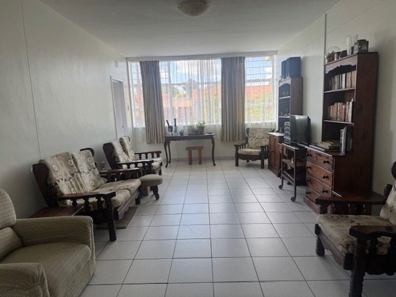 Spacious living room featuring neutral tiled flooring and a large window with security bars, providing ample natural light.