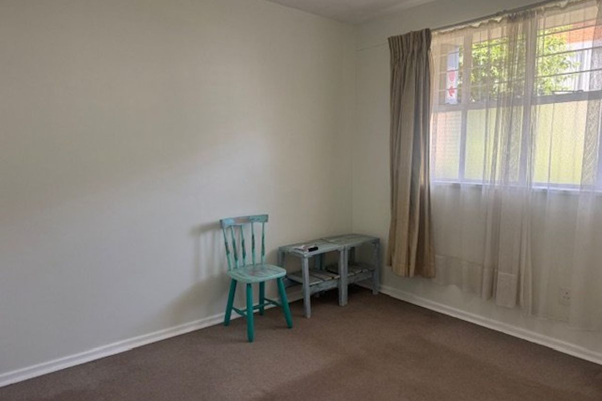 A simple, carpeted bedroom featuring a window with security bars and neutral wall finishes, offering a blank canvas for personalization.