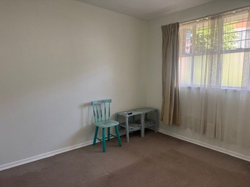 A simple, carpeted bedroom featuring a window with security bars and neutral wall finishes, offering a blank canvas for personalization.