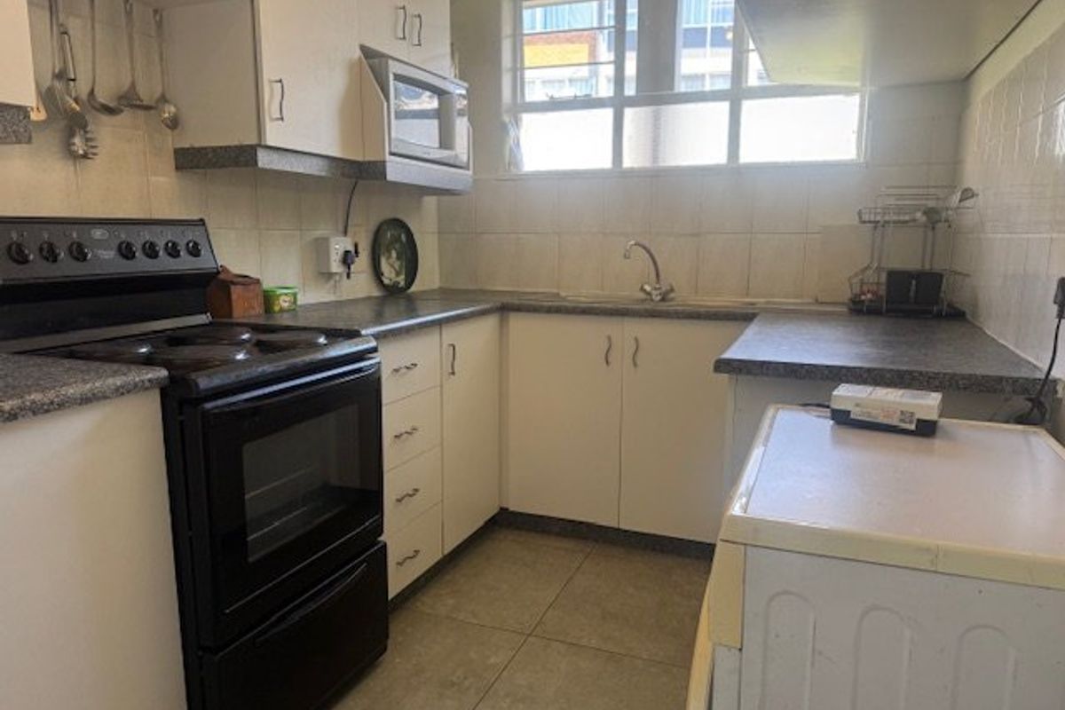 A functional kitchen featuring built-in cabinetry, laminate countertops, a tiled backsplash, and a freestanding stove, offering potential for modernization.
