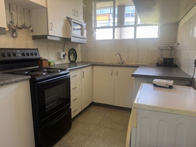 A functional kitchen featuring built-in cabinetry, laminate countertops, a tiled backsplash, and a freestanding stove, offering potential for modernization.