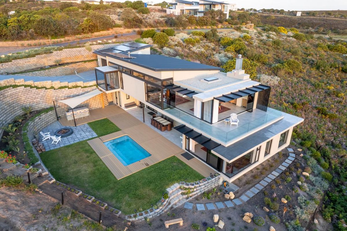 Aerial view of a modern multi-level residence featuring a swimming pool, expansive decking, terraced landscaping, and a large upper-level balcony with glass balustrades.