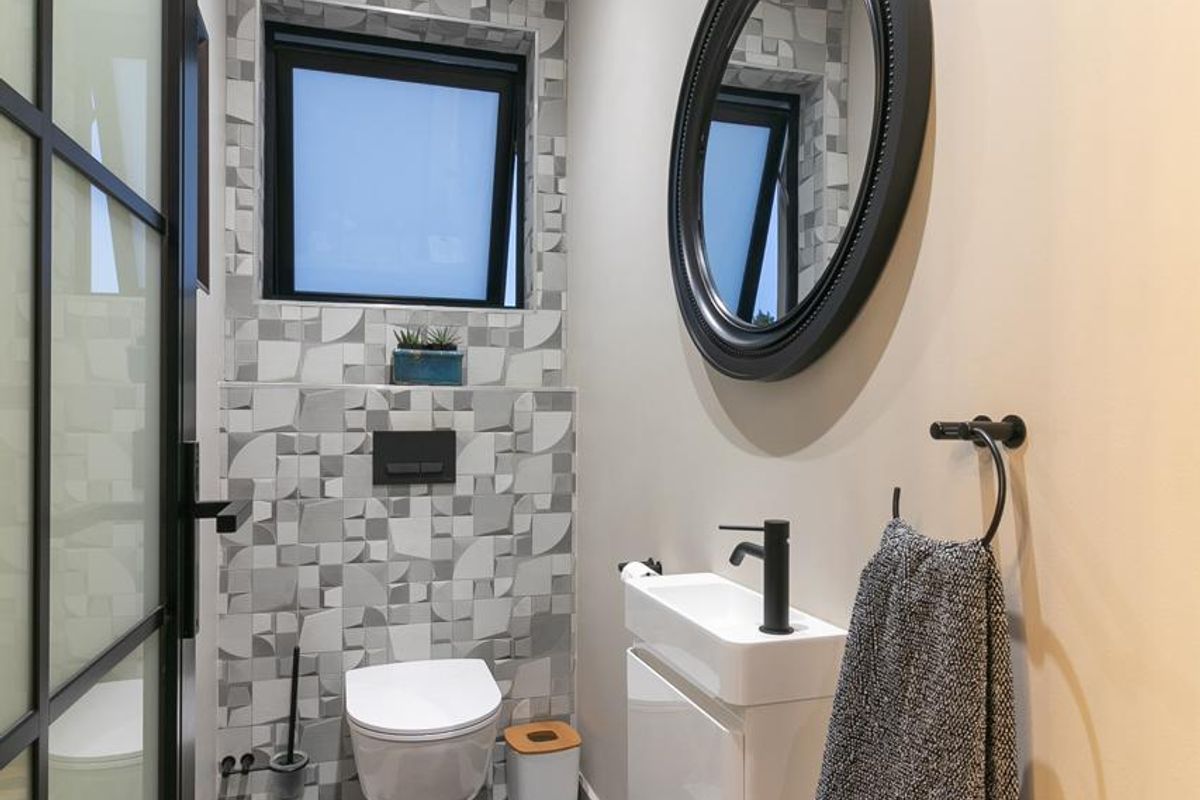 Modern guest bathroom featuring a wall-hung toilet, sleek vanity basin with black fixtures, and stylish geometric tiled feature wall.