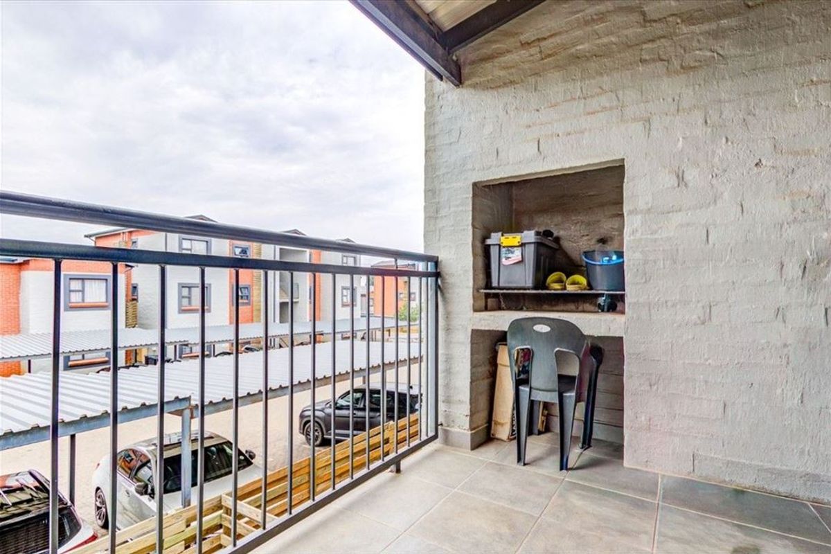 A covered balcony featuring a built-in brick niche, tiled flooring, and metal railings, overlooking the complex parking area.
