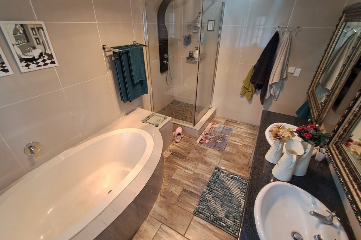 A well-appointed bathroom featuring a built-in bathtub, a separate glass-enclosed shower with a modern panel, and a vanity with a dark countertop.