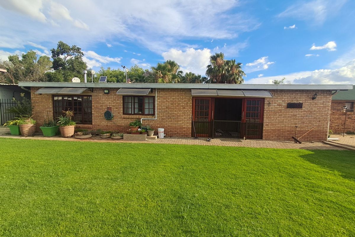 Rear view of a single-story face brick house featuring a paved patio area and a well-maintained lawn.