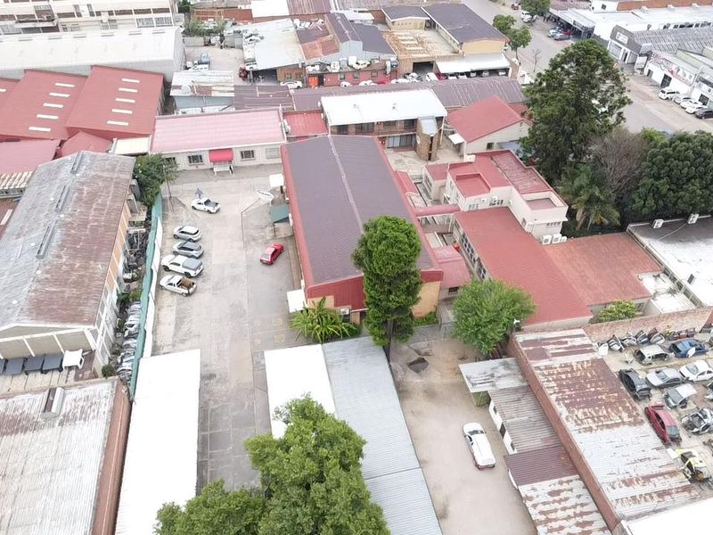 Aerial view of an industrial property complex featuring multiple buildings with metal roofing, paved yard areas, and covered parking facilities.
