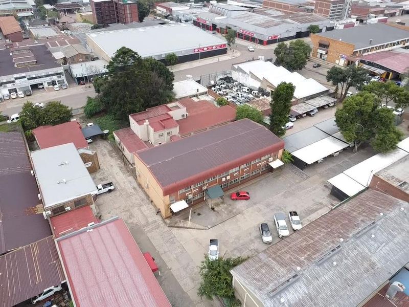 Aerial view of an industrial property featuring a main building with a metal roof, paved yard area, and multiple covered parking bays.