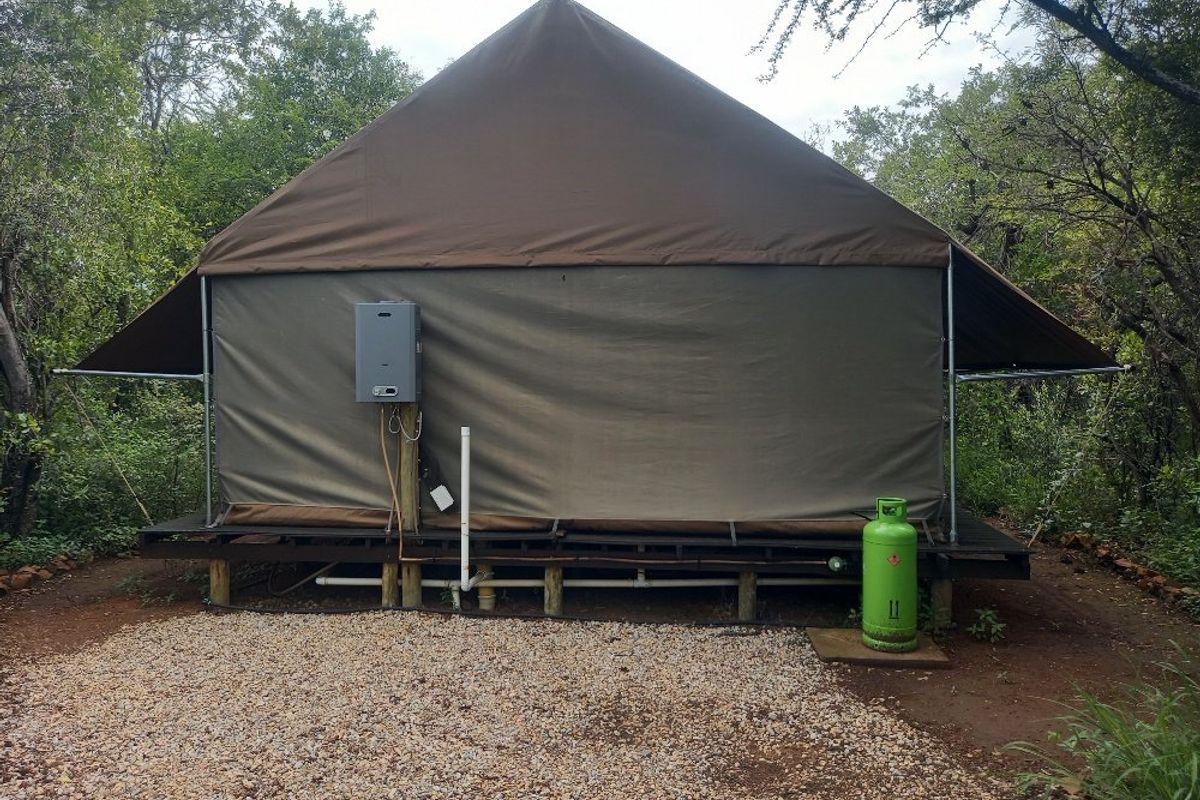 Rear view of a canvas tent structure on a raised timber deck, featuring an external gas geyser and gas supply installation.