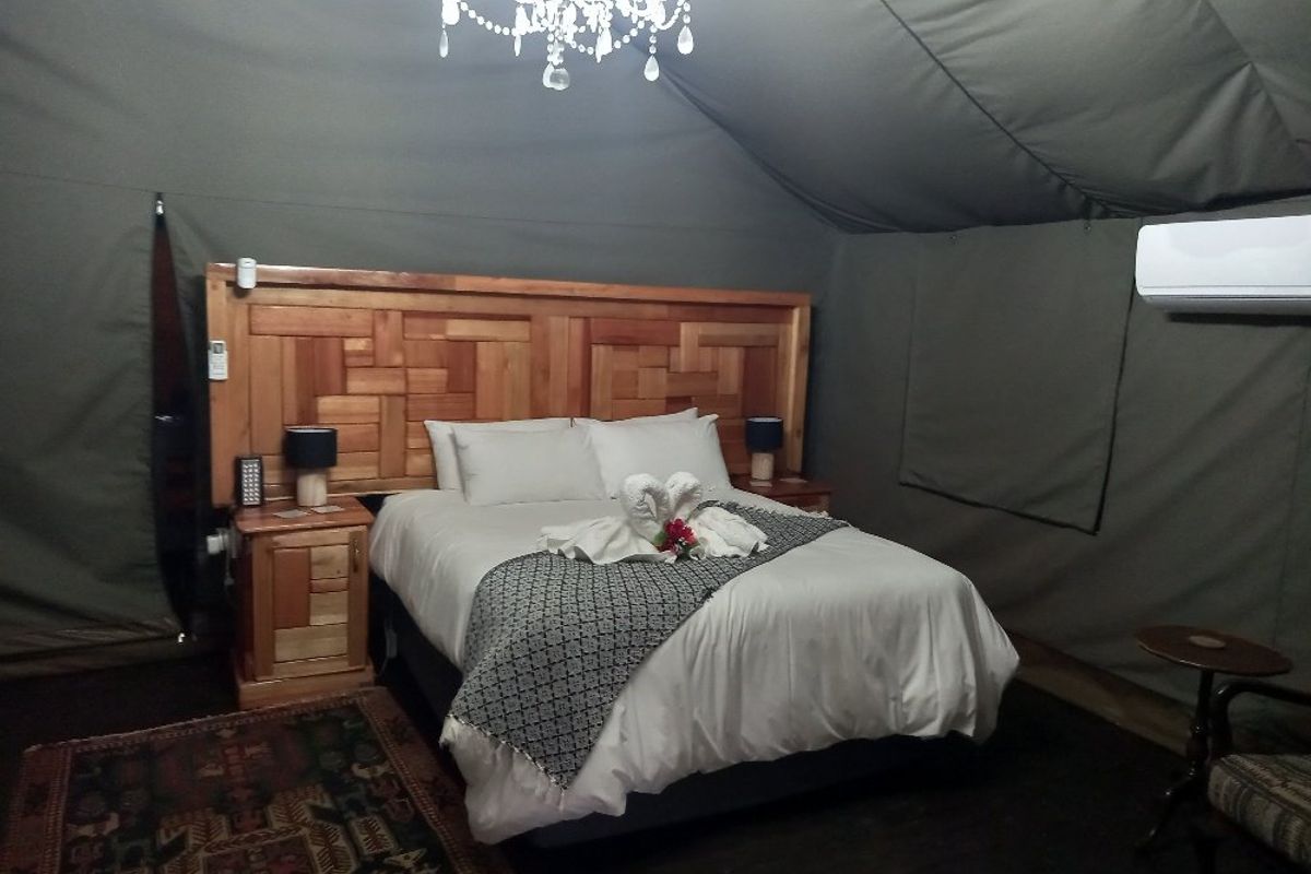 A luxury tented bedroom suite featuring a custom timber headboard, canvas walls, and a split-system air conditioning unit for climate control.