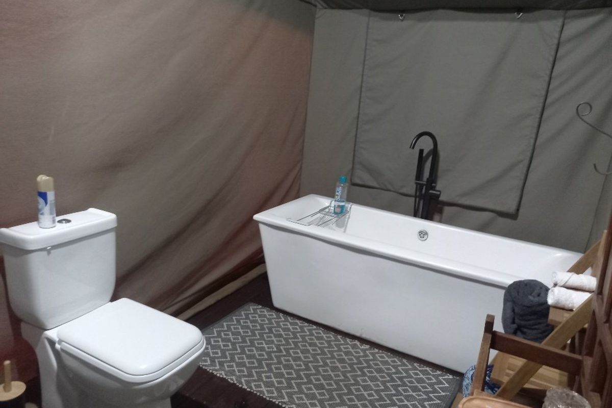 A bathroom area within a tented structure featuring a modern white freestanding bathtub with a black mixer tap and a standard toilet.