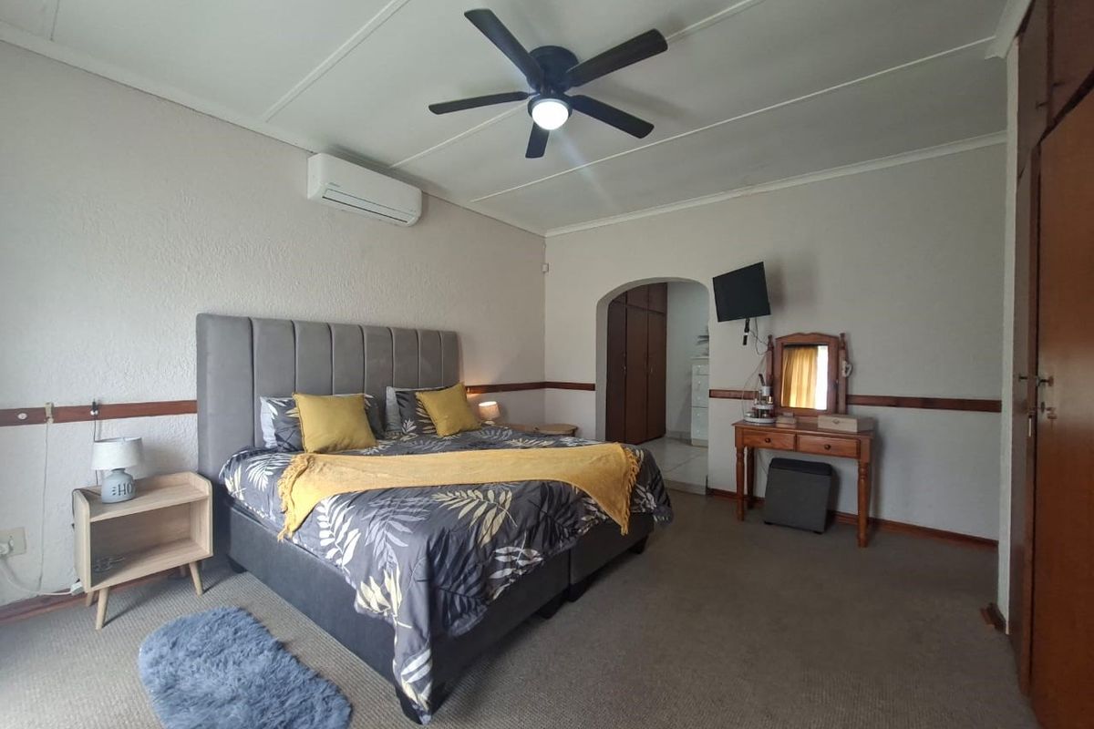 Spacious bedroom featuring a ceiling fan, wall-mounted air conditioning unit, and built-in wooden cabinetry with an arched entryway.