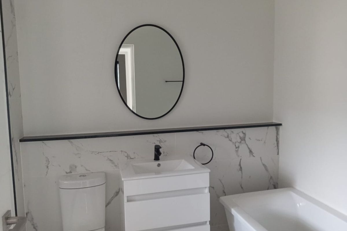 Modern bathroom featuring a white vanity, black tapware, marble-look wall tiles, a freestanding bathtub, and a sleek black-framed oval mirror.