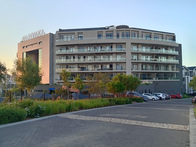 A modern multi-story apartment building exterior featuring glass balconies, a paved driveway, and landscaped surroundings at the Munyaka estate.