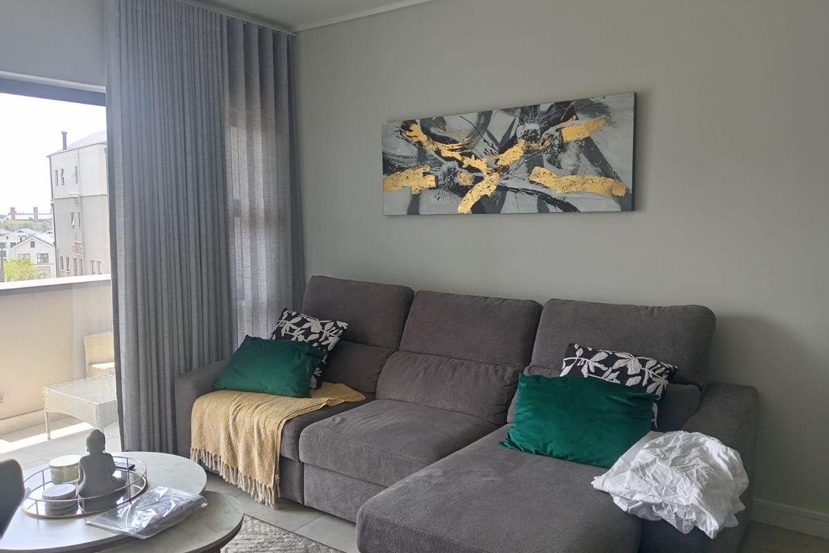 A well-maintained living room featuring neutral walls, tiled flooring, and a large sliding glass door providing access to a balcony.