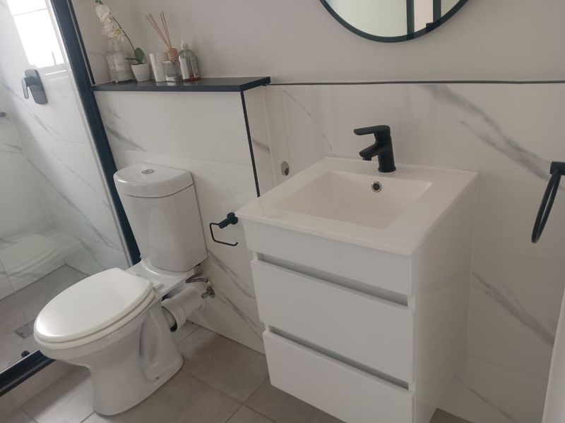 Modern bathroom featuring a white vanity with black mixer tap, marble-look wall tiling, and a glass-enclosed shower.
