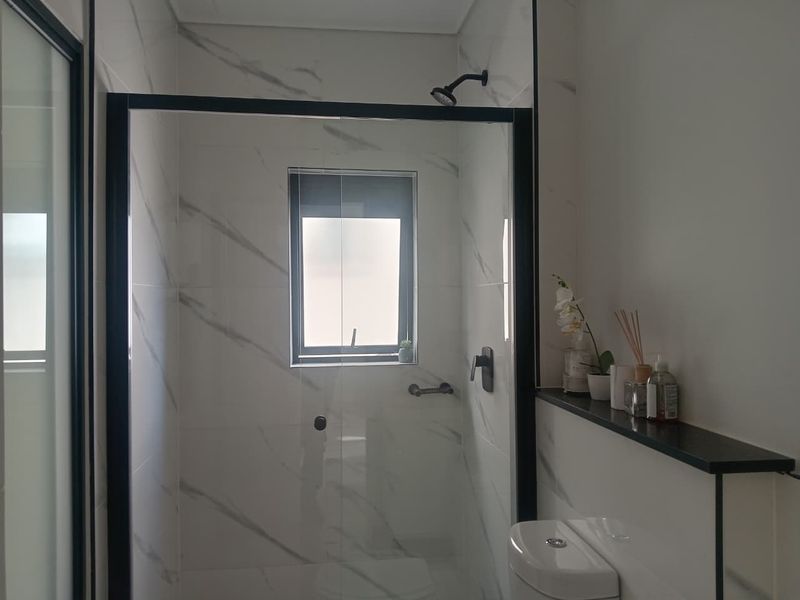 Modern bathroom featuring a walk-in shower with black frame, marble-look wall tiles, and a built-in shelf above the toilet.