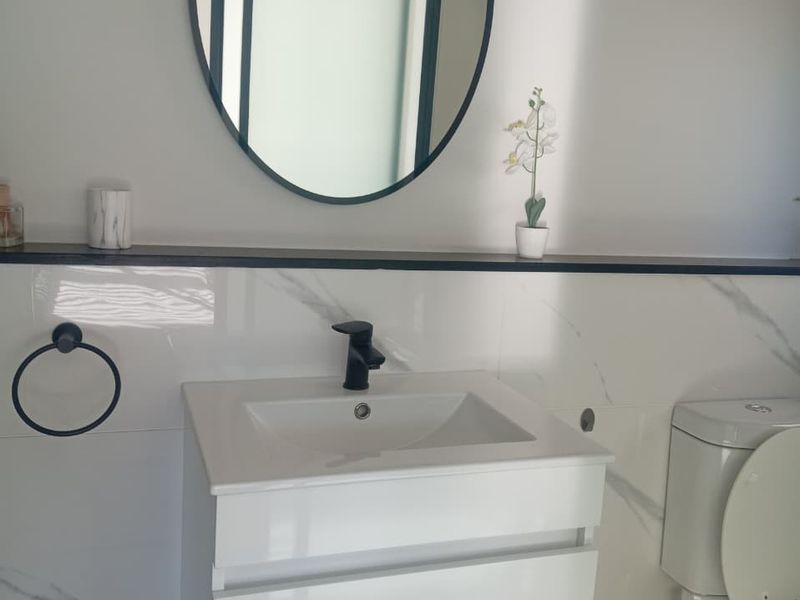 Modern bathroom featuring a sleek white vanity cabinet, black fixtures, a contemporary oval mirror, and elegant marble-look wall tiling.