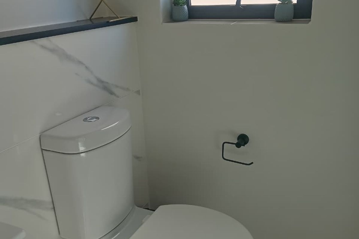 A modern bathroom featuring a white toilet, marble-look wall tiling, and a black-framed window.