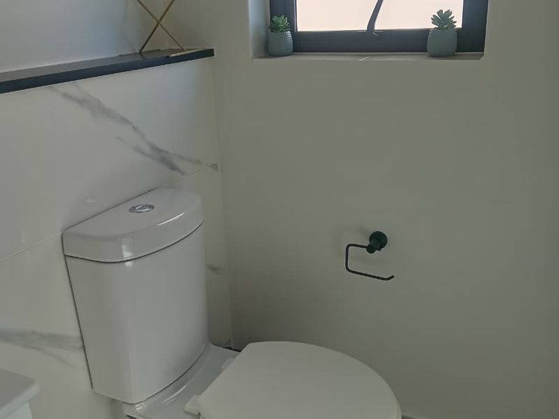A modern bathroom featuring a white toilet, marble-look wall tiling, and a black-framed window.