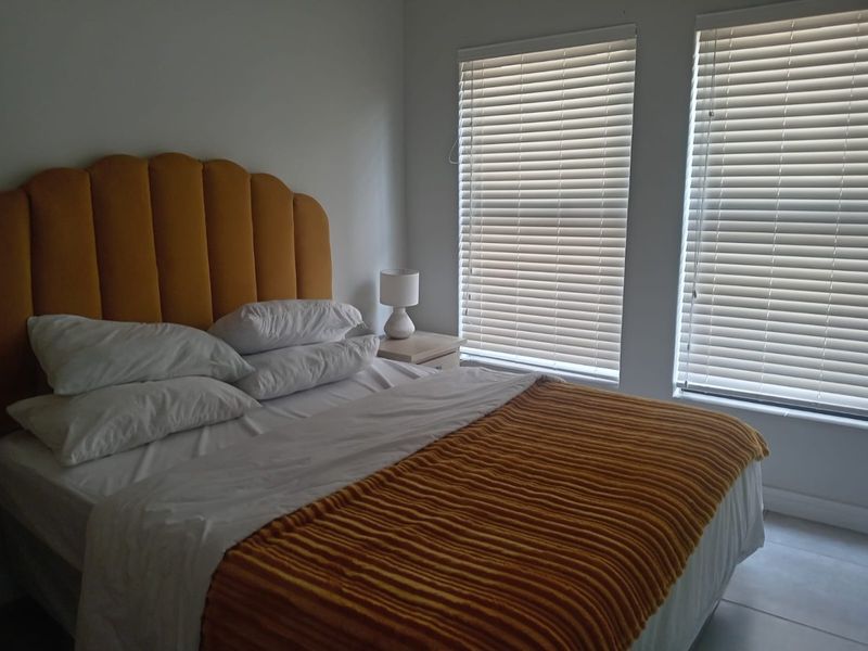 A well-lit bedroom featuring neutral tiled flooring and dual windows fitted with white venetian blinds.