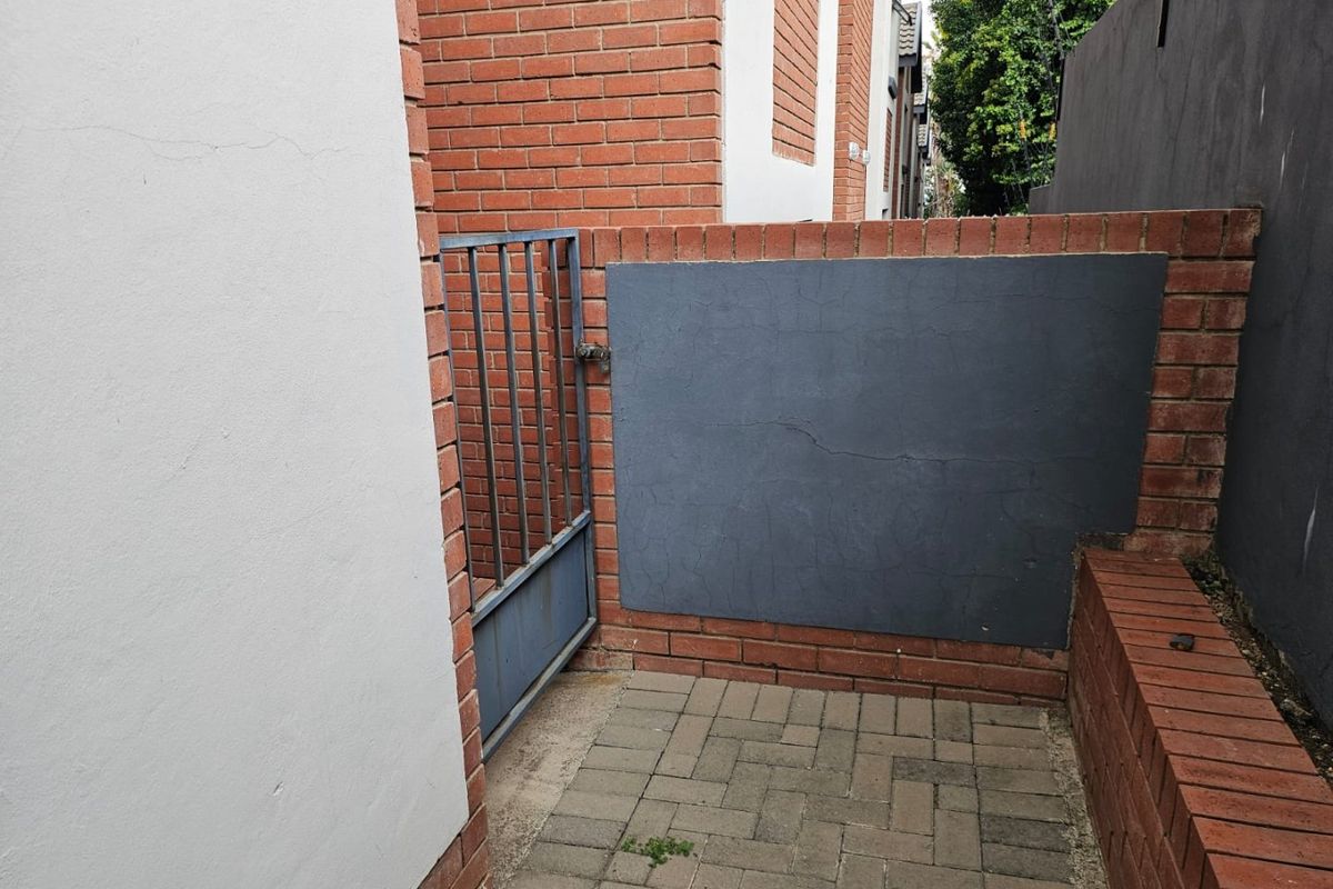 A side access area featuring a paved walkway, brick boundary walls, and a metal pedestrian gate.