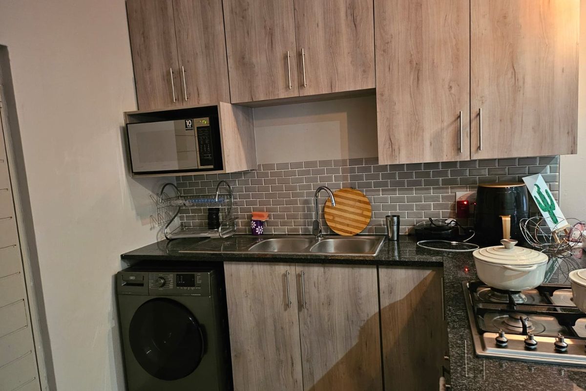 A functional kitchen featuring wood-look cabinetry, subway tile backsplash, granite-style countertops, a gas hob, and a built-in microwave with an integrated washing machine.