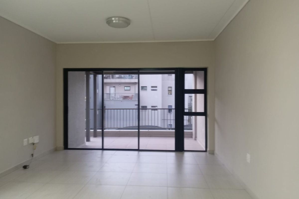 A bright, empty living room featuring neutral tiled flooring and a large sliding glass door leading to an outdoor balcony area.