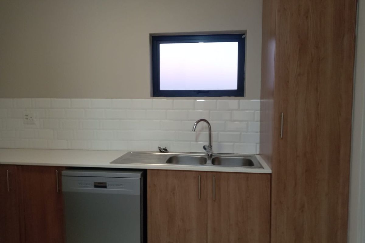 A clean, modern kitchen area featuring wood-look cabinetry, a double stainless steel sink, subway tile backsplash, and a tall built-in pantry cupboard.