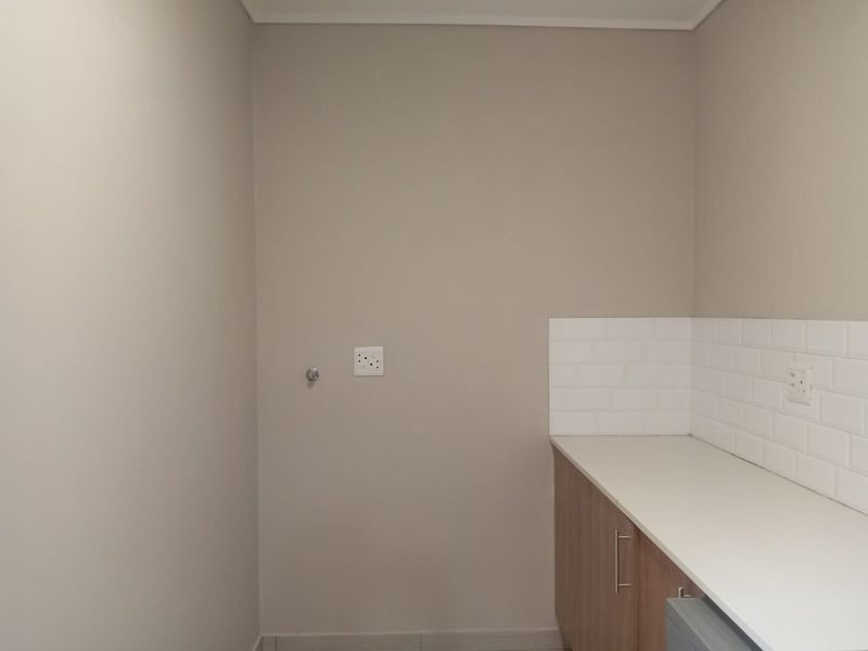 A clean, empty laundry area featuring built-in cabinetry, a white countertop, and a subway tile backsplash with dedicated plumbing and electrical connections.