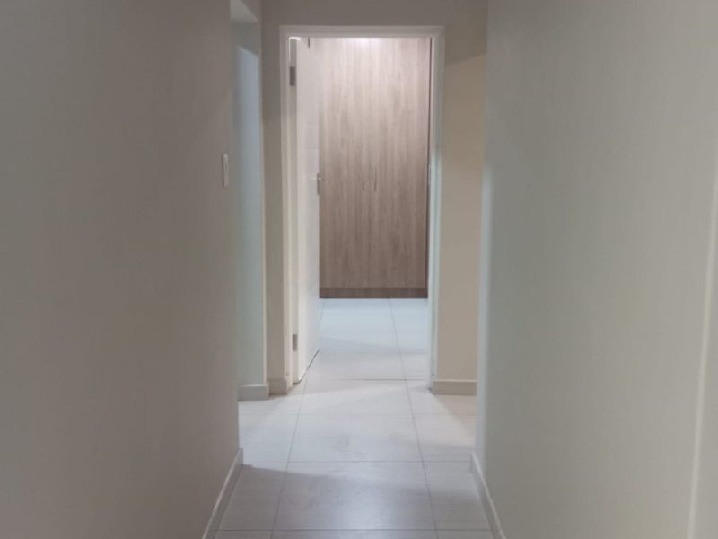A clean, neutral-toned hallway featuring light-colored floor tiles and a view through to a room with built-in wooden cabinetry.
