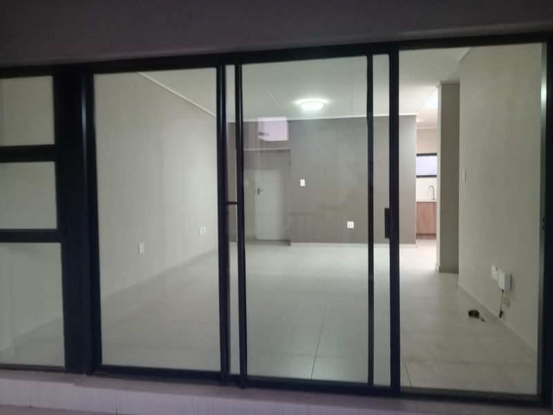 An open-plan living area featuring large sliding glass doors, neutral tiled flooring, and a glimpse into the adjacent kitchen space.