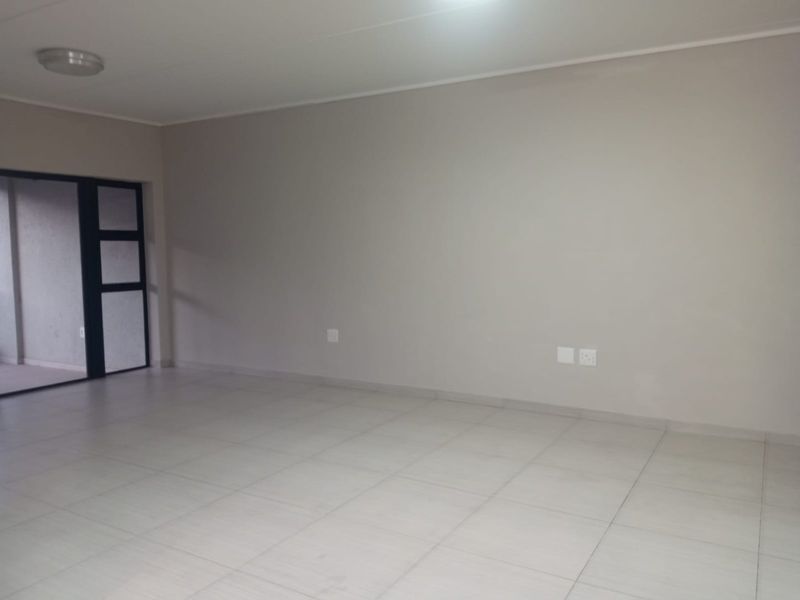 A spacious, empty living area featuring neutral tiled flooring and a sliding glass door providing access to an outdoor space.