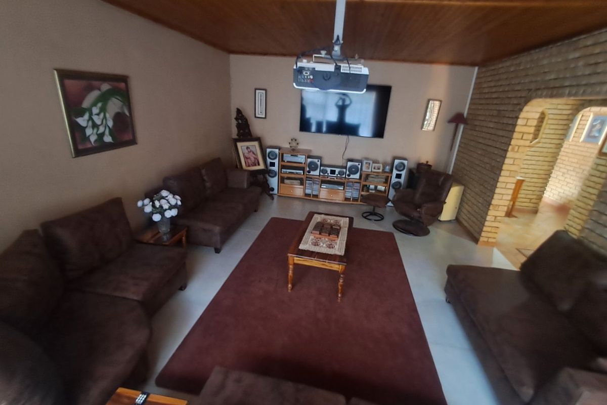 Spacious living room featuring a timber ceiling, exposed brick archway, and tiled flooring, currently set up as a home cinema area.