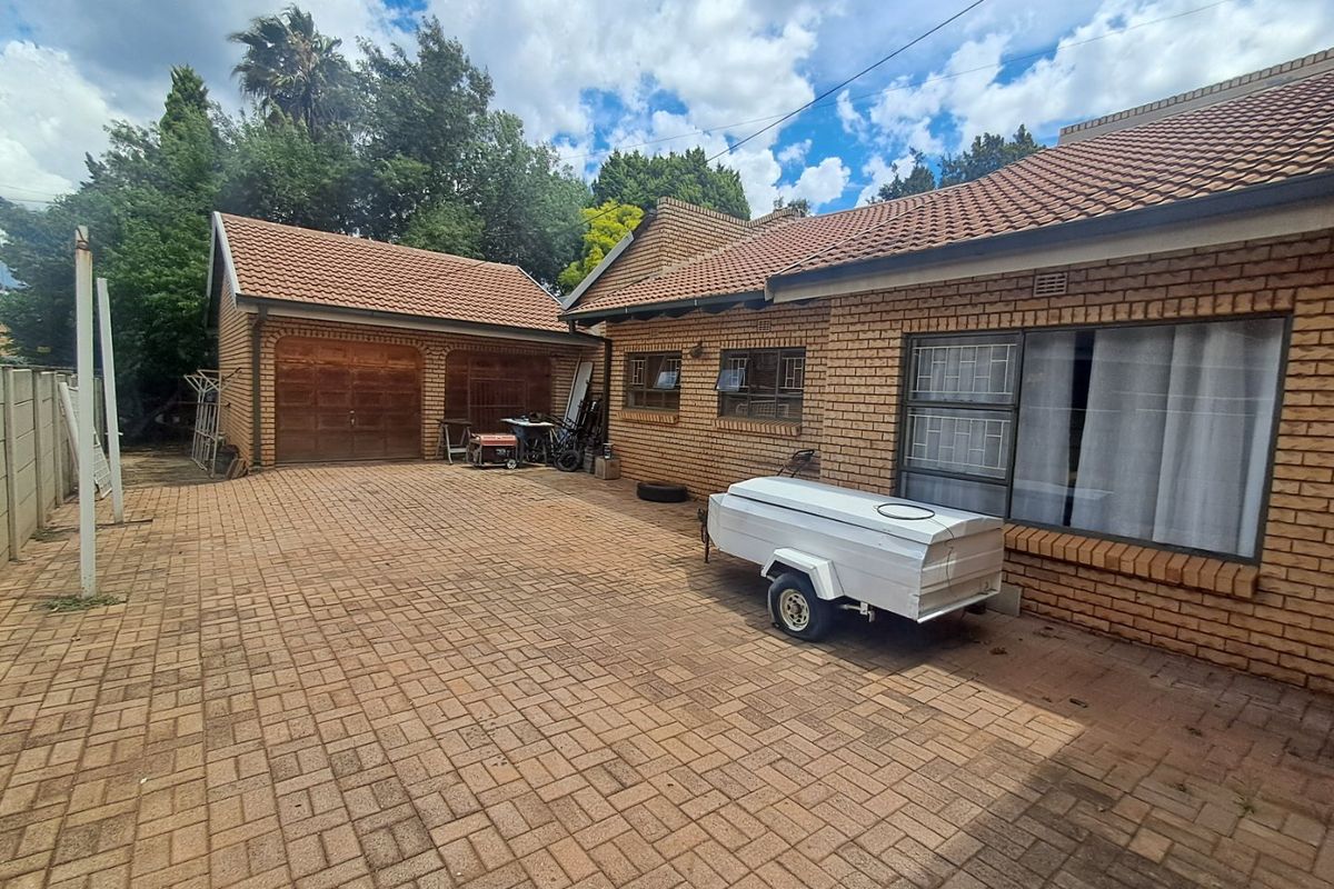 Rear exterior view featuring a spacious brick-paved courtyard, facebrick house facade, and a detached double garage with wooden doors.