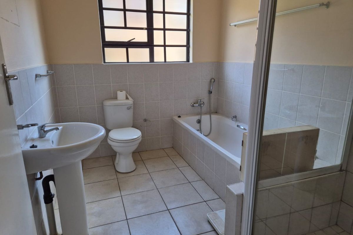 A functional bathroom featuring a pedestal basin, toilet, bathtub, and separate shower enclosure with neutral wall and floor tiling.