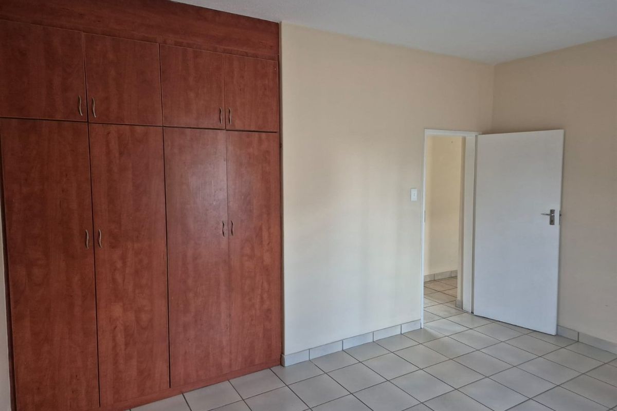 A clean, empty bedroom featuring built-in wooden cupboards and neutral tiled flooring, offering a blank canvas for personalization.