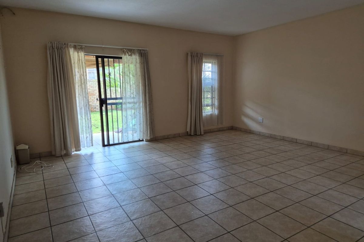 An empty, tiled living room featuring a sliding glass door with a security gate, providing direct access to the outdoor area.