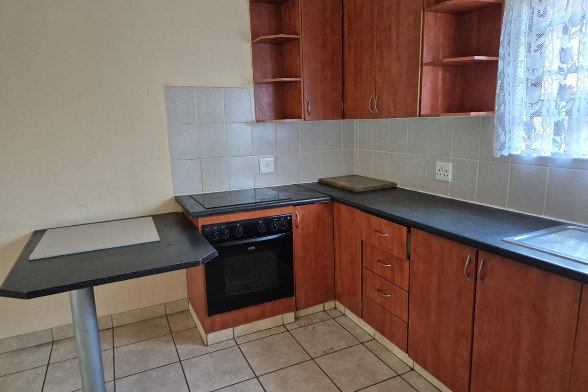 A functional kitchen featuring laminate cabinetry, built-in oven, electric hob, tiled backsplash, and a breakfast bar with tiled flooring.