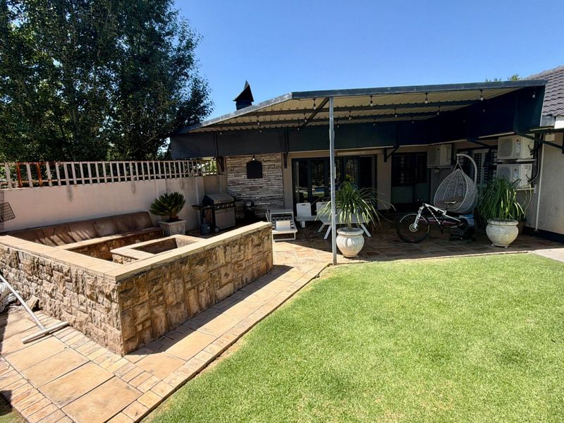 A spacious covered patio featuring a built-in stone fire pit, paved flooring, and direct access to the rear garden area.