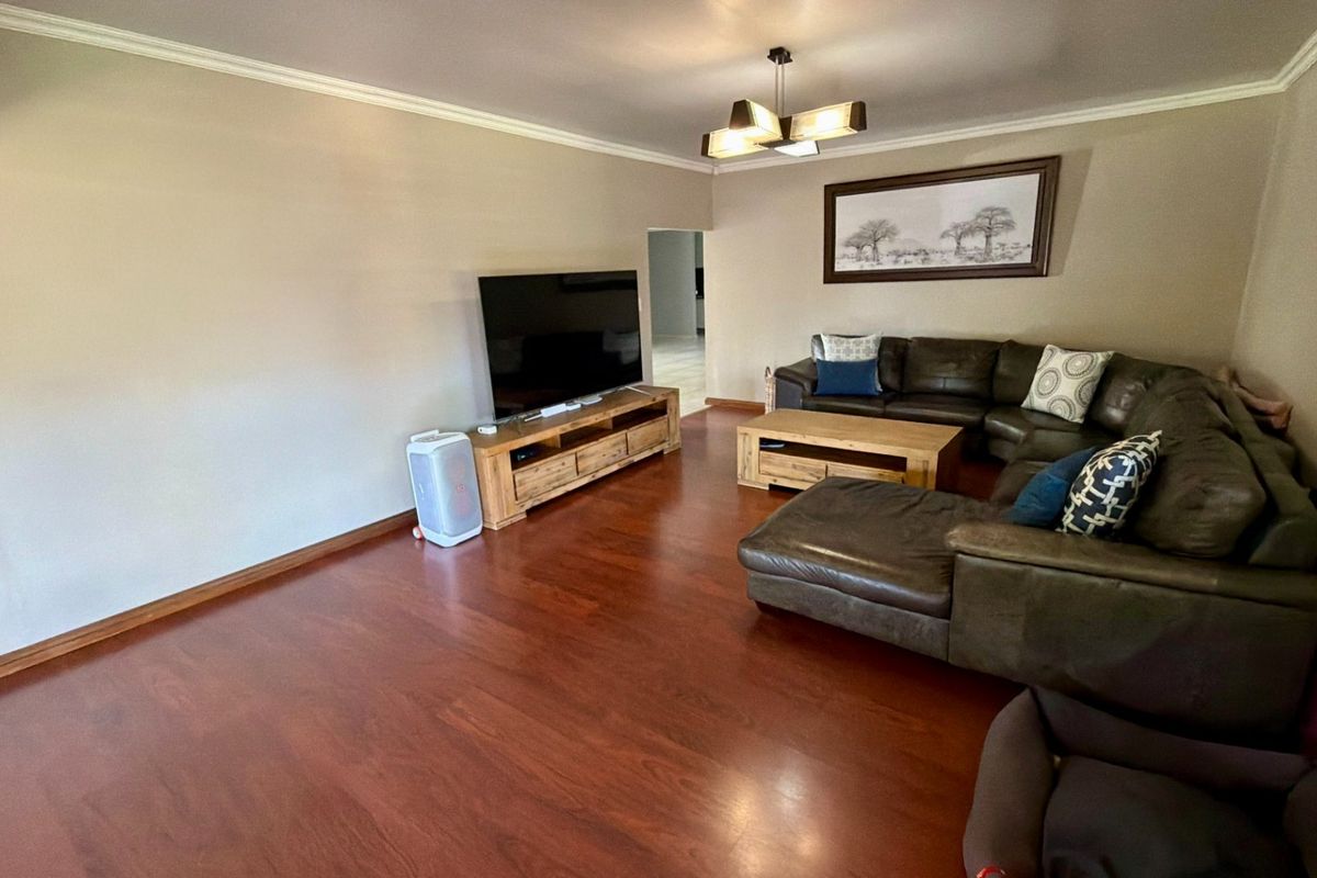 A spacious living room featuring warm-toned laminate flooring, cove cornicing, and a contemporary ceiling light fixture, offering a comfortable and well-maintained living space.