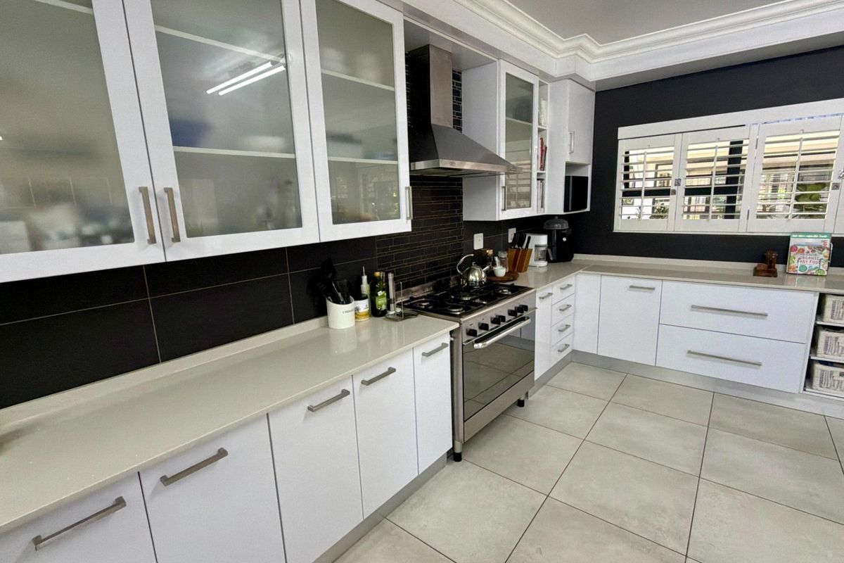 Modern kitchen featuring white cabinetry, quartz countertops, a gas stove with stainless steel extractor, and tiled flooring with plantation shutters.