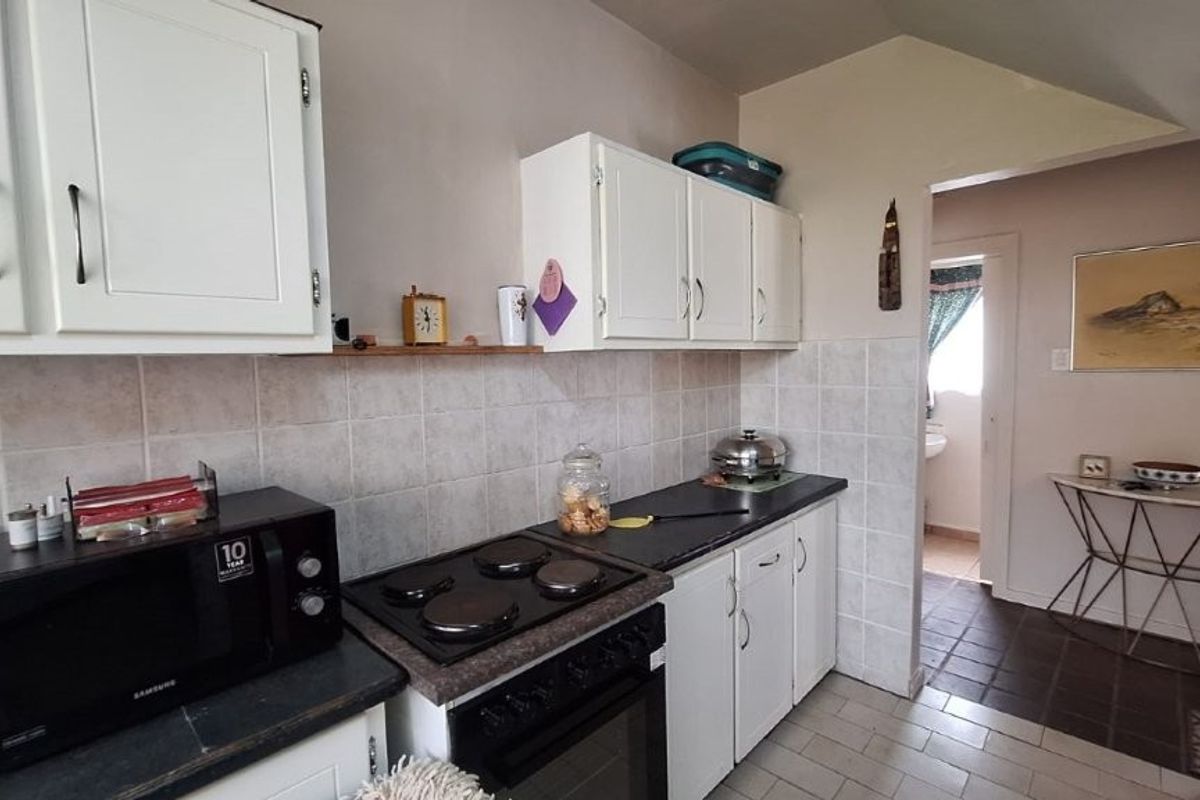 A functional kitchen featuring white cabinetry, tiled backsplash, and built-in electric cooking appliances, with direct access to an adjacent hallway.