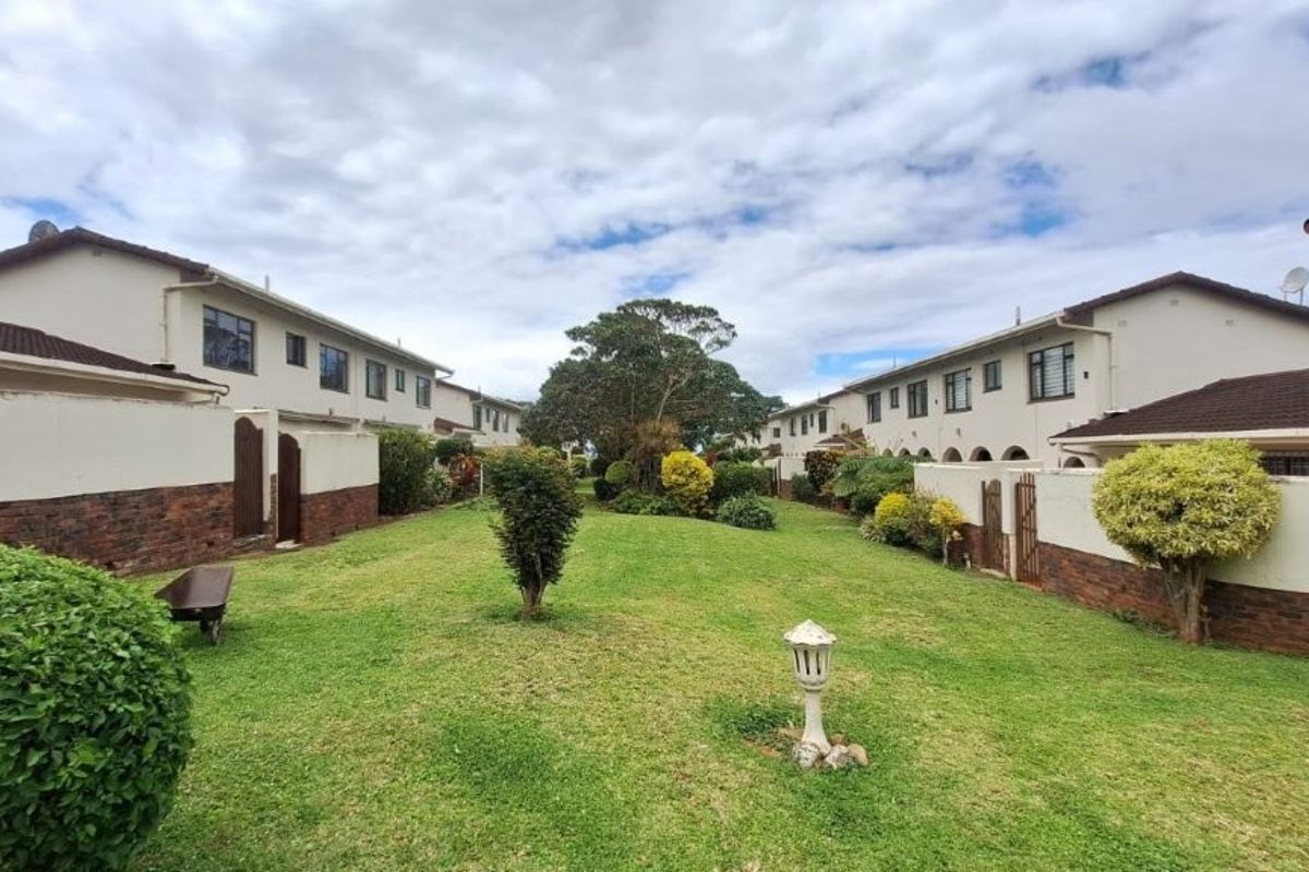 A view of the shared rear garden area between townhouse units, featuring well-maintained lawns and brick boundary walls.