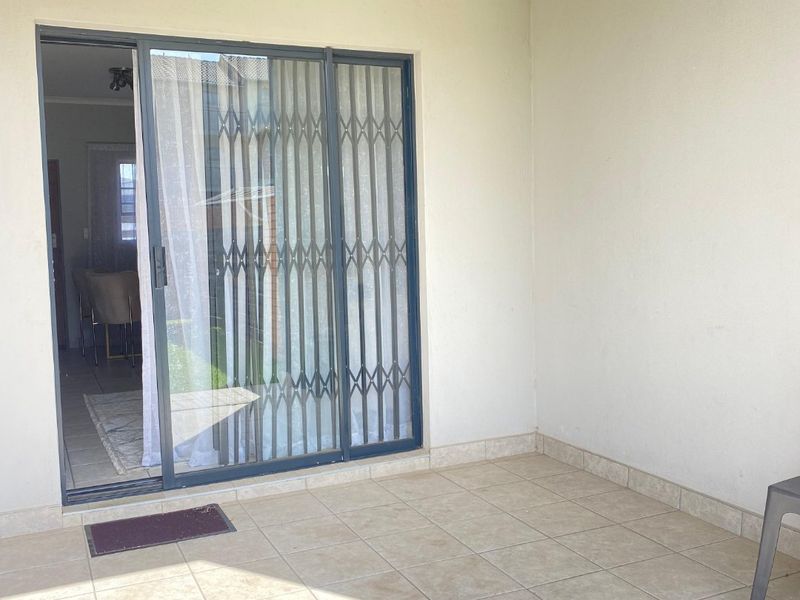 A covered patio area featuring tiled flooring and a sliding glass door with a security gate, providing direct access to the interior living space.