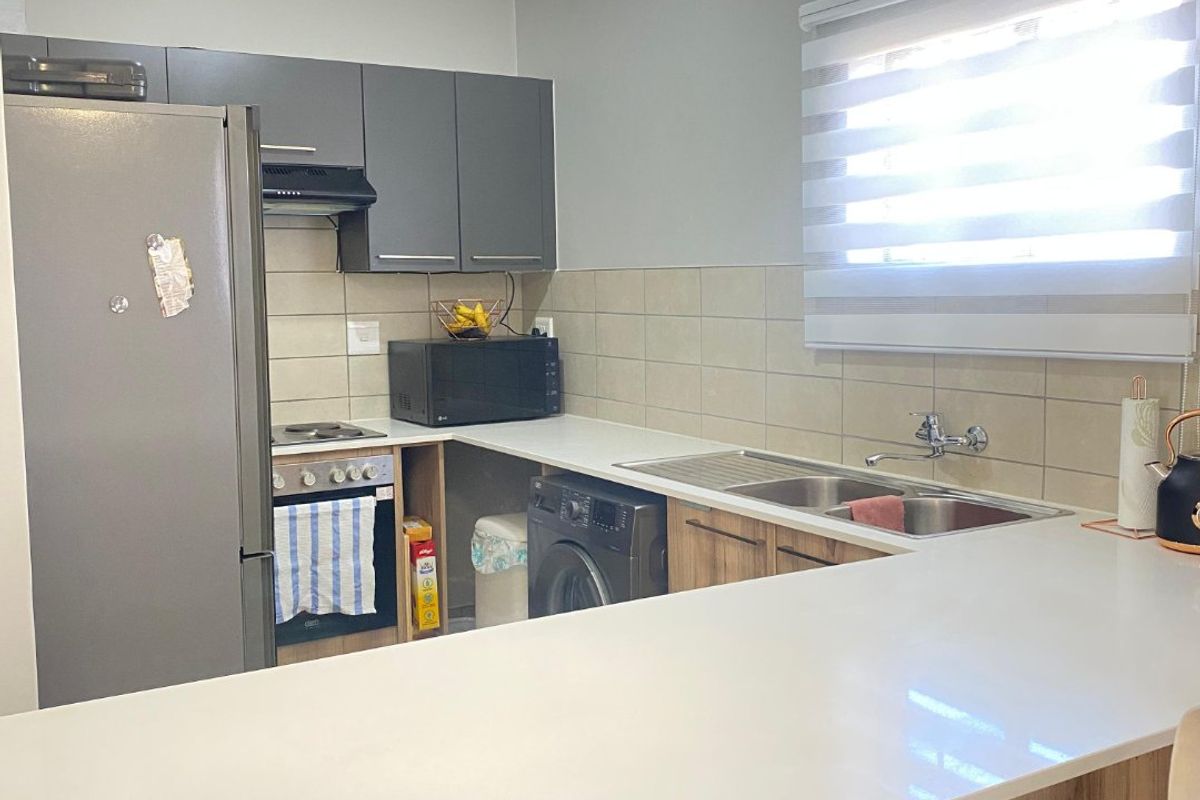 Modern kitchen featuring grey and wood-tone cabinetry, white quartz countertops, a breakfast bar, and integrated appliances including an oven and hob.