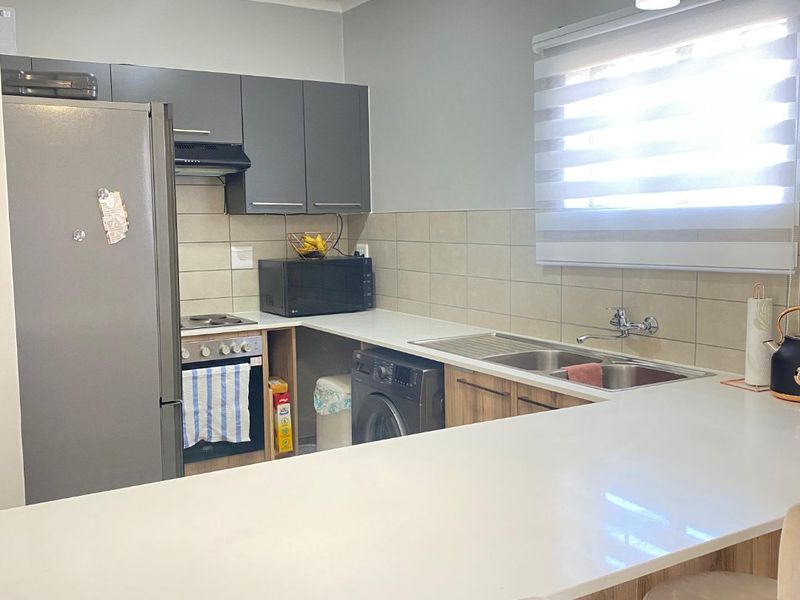 Modern kitchen featuring grey and wood-tone cabinetry, white quartz countertops, a breakfast bar, and integrated appliances including an oven and hob.