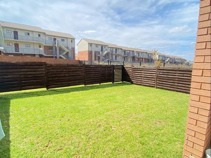 A private rear garden featuring a well-maintained lawn, timber slat fencing, and a tiled patio area adjacent to the brick building structure.
